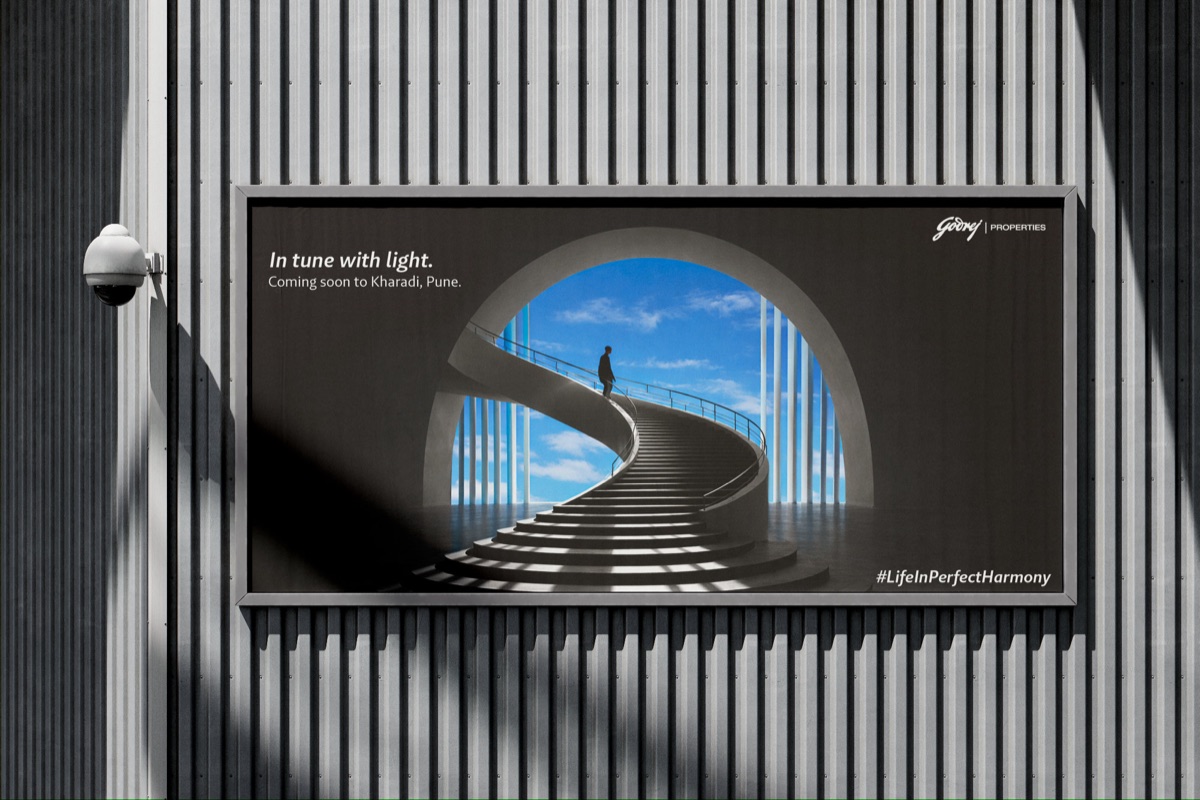 Outdoor billboard reading “In tune with light” — a curving staircase rising under an arch into blue sky.