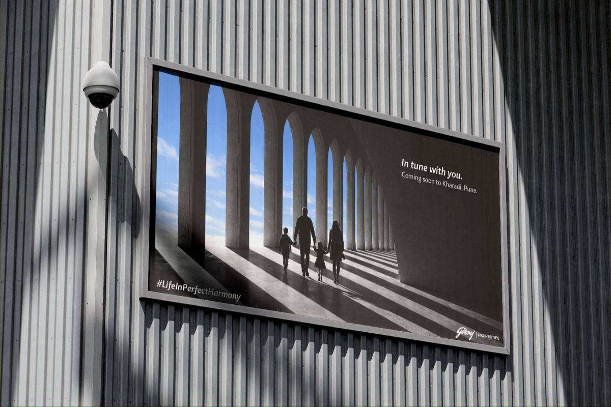 Outdoor billboard reading “In tune with life” — two figures walking a long colonnade in raking shadow.