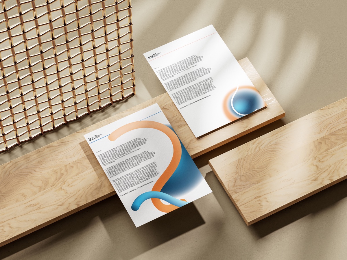 Letterheads laid across wooden boards beside a woven mat, each showing the flowing gradient mark.